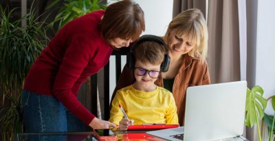 Child learning online with supportive adults at home, using a laptop and tablet.