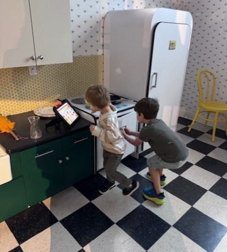Kids playfully cooking in a colorful kitchen, using a tablet for imaginative recipes.