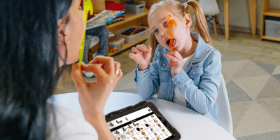 Child engages with teacher using a Quicktalker Freestyle AAC device for interactive learning and playtime activities.