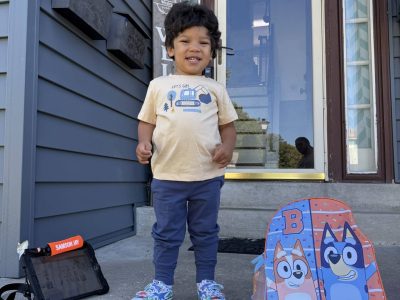 Happy little boy standing on porch with backpack and tablet, ready for adventure.