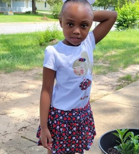 Little girl in a summer dress poses outdoors with a playful expression.