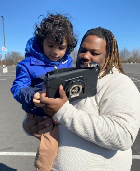 Parent and child exploring educational content on a tablet outdoors in the parking lot.